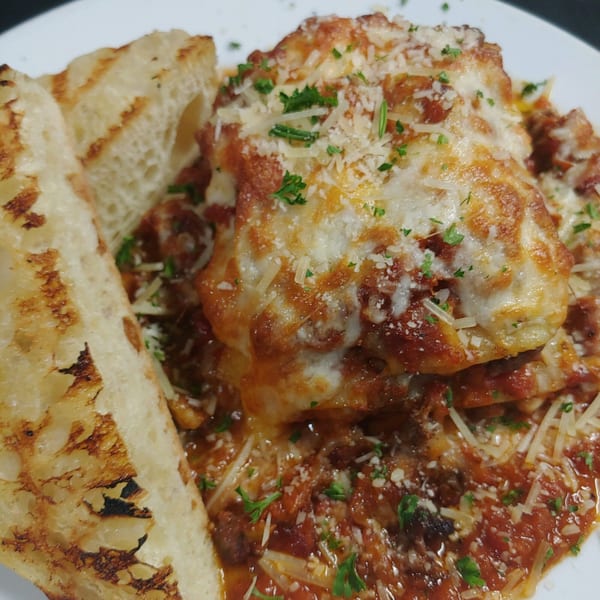 Southern-style lasagna with melted cheese, tomato sauce, and parsley, served with grilled bread.