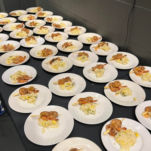 Numerous plates of southern shrimp skewers and risotto with corn and squash on a black table.