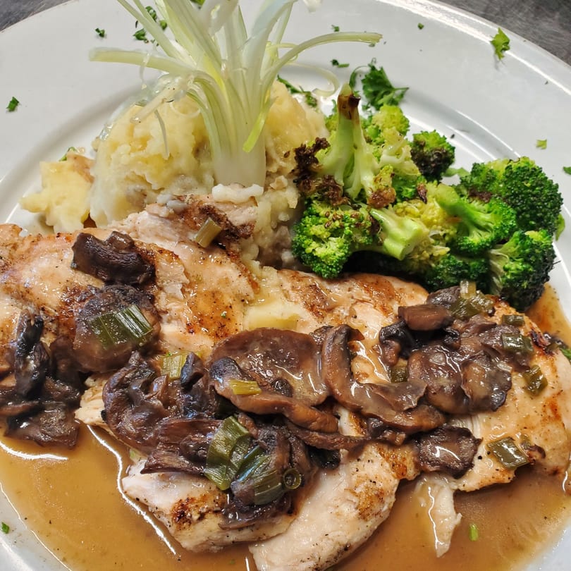 Chicken with mushroom gravy, mashed potatoes, and broccoli, garnished with scallions on a white plate.