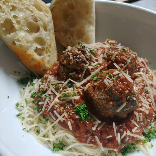 Spaghetti with meatballs, red sauce, parmesan cheese, and parsley, served with two slices of garlic bread.