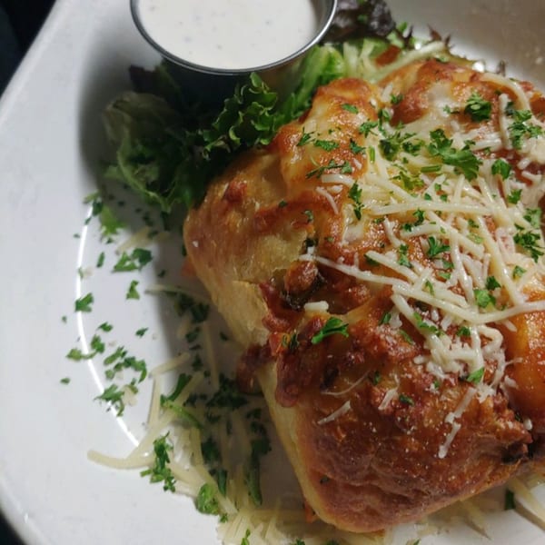 Golden-brown baked bread topped with melted cheese and parsley, served with a side of ranch dressing.