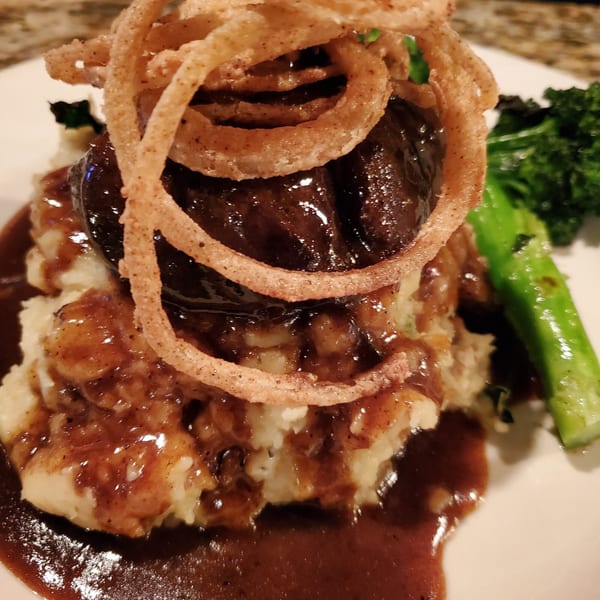 Southern-style short ribs on mashed potatoes with gravy, topped with crispy fried onions and a side of broccoli.