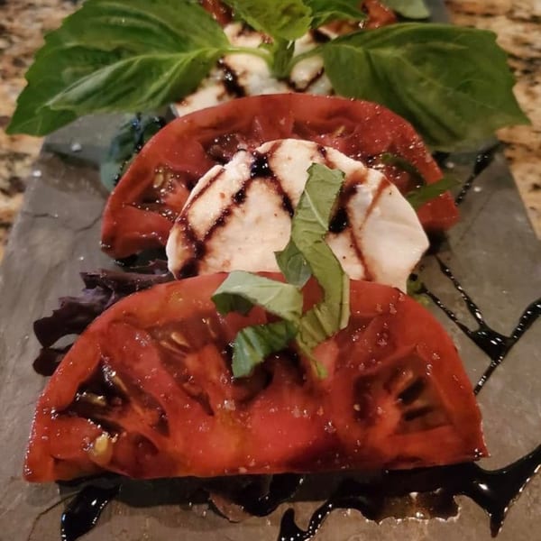 Caprese salad with sliced tomatoes, mozzarella, basil, and balsamic glaze on a dark plate.