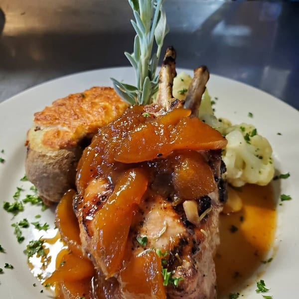 Southern-style pork chop with peach glaze, baked potato, and cauliflower on a white plate.
