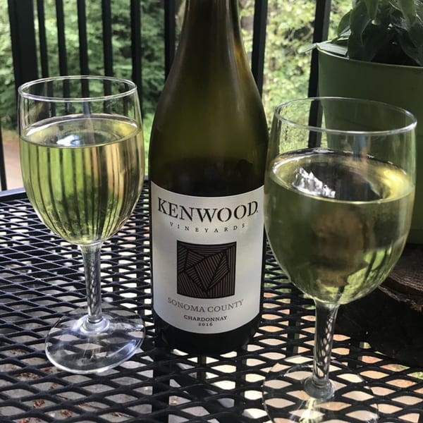 Two glasses of white wine and a bottle of Kenwood Vineyards Chardonnay on a black patio table.