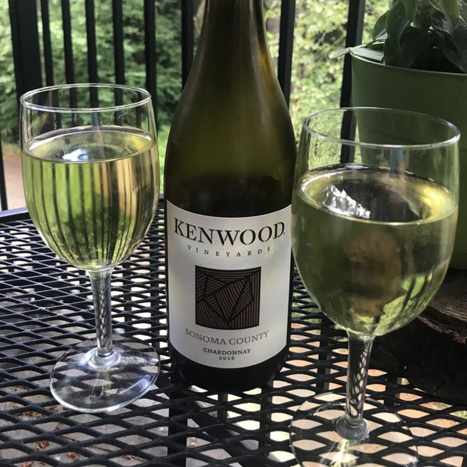 Two glasses of white wine and a bottle of Kenwood Vineyards Chardonnay on a black patio table.