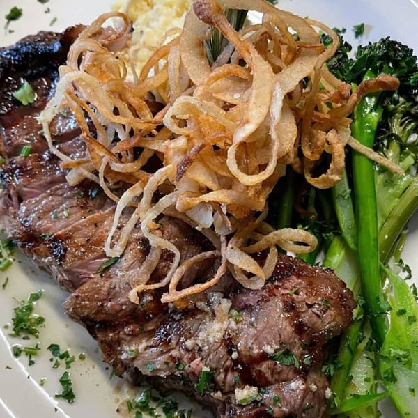 Southern-style steak with crispy fried onions, mashed potatoes, and green broccoli on a white plate.