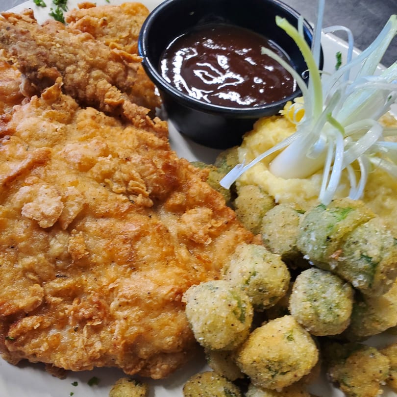 Crispy fried chicken, mashed potatoes, fried okra, and BBQ sauce garnished with green onions.