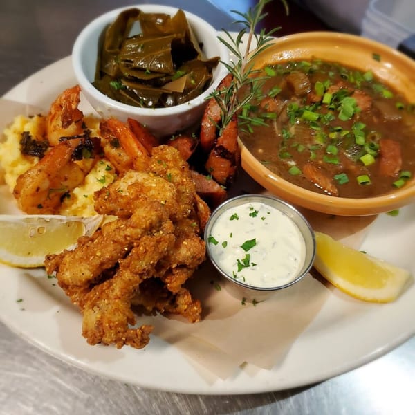 A southern meal with fried shrimp, grits, gumbo, collard greens, and tartar sauce.