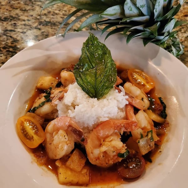 Southern-style shrimp and rice dish with pineapple, cherry tomatoes, and a basil leaf garnish.