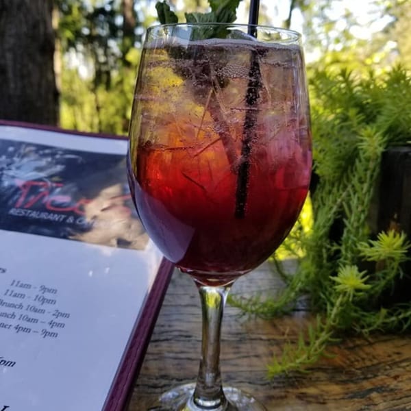 A refreshing red drink with ice and mint, next to a menu on a wooden table outdoors.