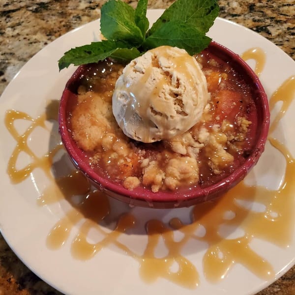 Southern peach cobbler with a scoop of vanilla ice cream, caramel drizzle, and mint garnish.