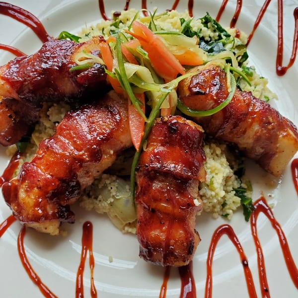 Bacon-wrapped southern chicken with a sweet glaze, served over couscous and mixed vegetables.