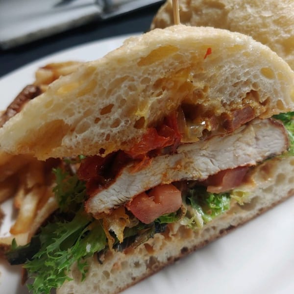 Close-up of a southern fried chicken sandwich with lettuce, tomato, and sauce on ciabatta bread.